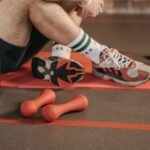 Detail view of a workout setup with dumbbells, shoes, and gym accessories on a yoga mat.