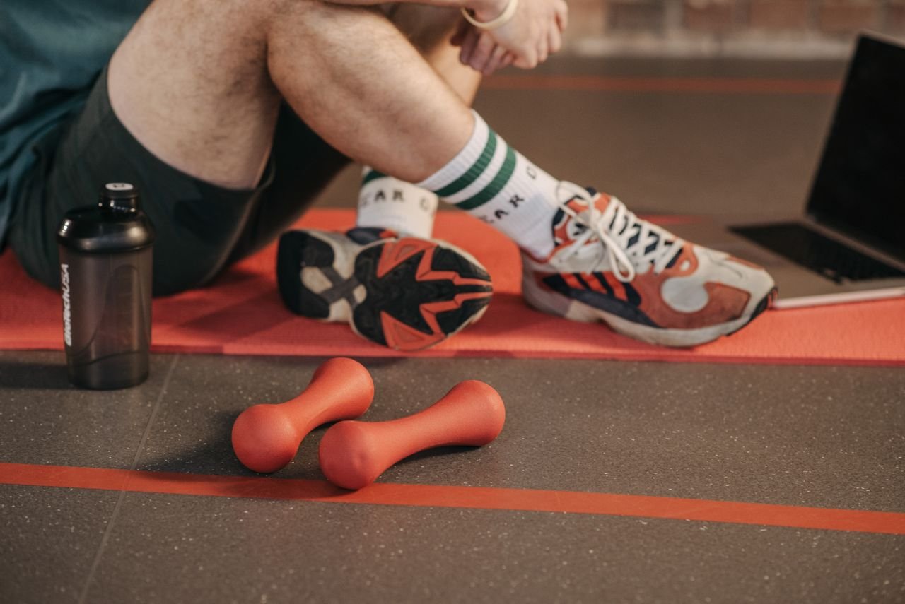 Detail view of a workout setup with dumbbells, shoes, and gym accessories on a yoga mat.